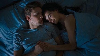 Top View Bed at Night: Attractive young Couple Sleeping Together, Holding Each other in Arms, Embracing. First Rays of Morning Sun Illuminate Room Trough the Window