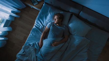 Top View of Handsome Young Man Sleeping Cozily on a Bed in His Bedroom at Night. Blue Nightly...