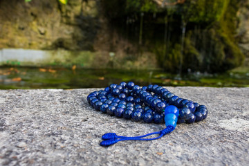 Blue mala beads on stone with water font in the background, close up and selective focus.