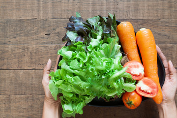 Top view woman's hands holding a plate of fresh vegetables