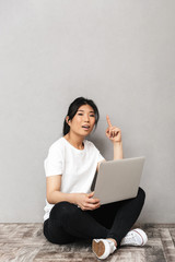 Asian beautiful young woman posing isolated over grey wall background using laptop computer.