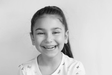 Portrait of happy smiling child girl on light background. Positive emotions. Black and white image.