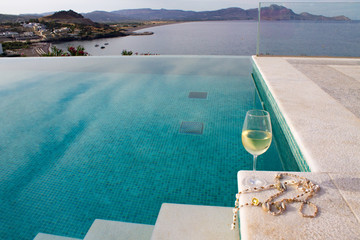 glass of white wine with shell beads is located on the edge of the pool stairs