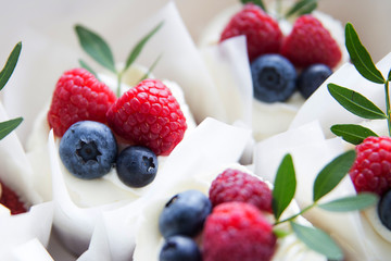 Appetizing cupcakes with white cream, raspberries and blueberries decorated with green leaves.