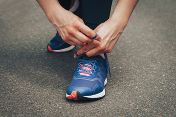 Evening run. Young lady running on a rural road during sunset in blue sneakers. Girl tying shoelaces before running