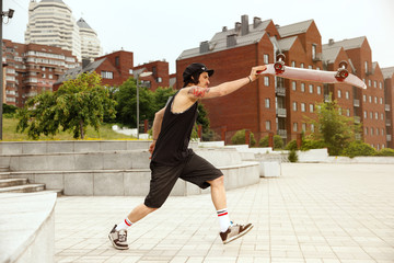 Skateboarder doing a trick at the city's street in cloudly day. Young man in sneakers and cap...