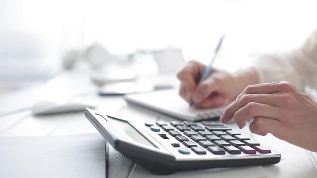  The hands of an accountant work on a calculator and prepare a financial report.