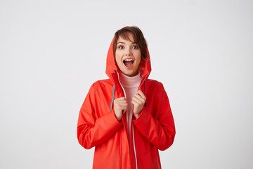 Portrait of young nice happy amazed short haired lady in red rain coat, looking at the camera with...