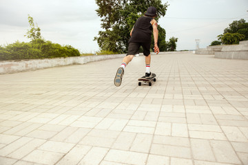 Skateboarder doing a trick at the city's street in cloudly day. Young man in sneakers and cap...