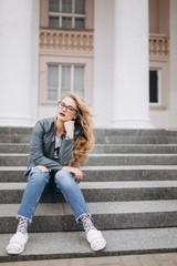 Young caucasian blondie hipster woman with long curly hairstyle in eye glasses in the city street. Freelance, freedom, beauty, happy lifestyle concept