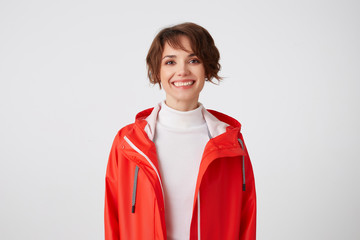 Portrait of young broadly smiling cute short haired girl dressed in white golf and red rain coat,...