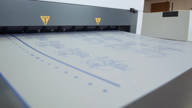 Printed sheet of paper coming out from printing machine. Offset printing, CMYK, close up