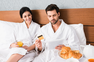 selective focus of man with credit card using digital tablet near happy woman