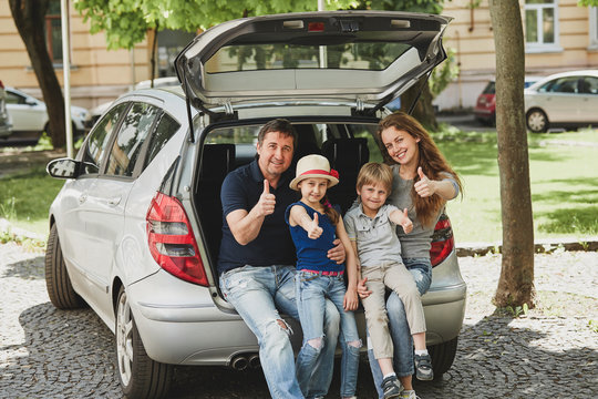 Family Sitting In The Trunk Of A Family Car And Showing Thumbs Up