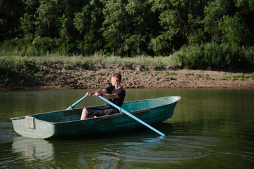 Young man floats on a wooden boat with oars