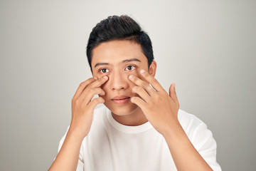 Closeup portrait of smiling adult Asian business man pointing to his eye and touching cheek. Isolated front view on white background.