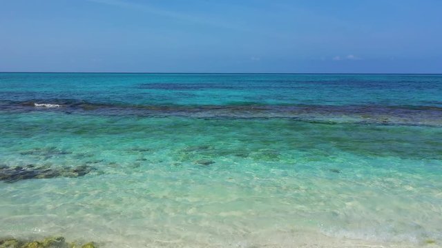 drone trucking right shot of wavy crystal clear water with coral and white sand, shallow water of Thailand sea