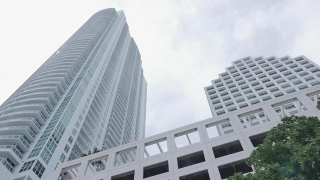 Skyscraper Slow Motion in low angle in Miami brickell business district the day. Cloudy sky, clouds, white. Car Point of View, Palm trees, sun light flare. Trees in foreground.