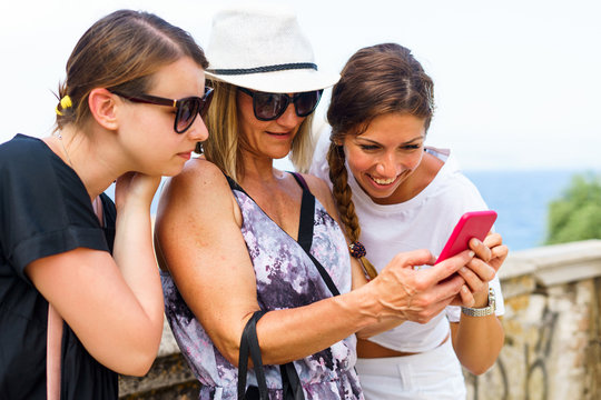 Three woman looking to the smart-phone mobile phone searching for the tourist information photos in the Corfu town