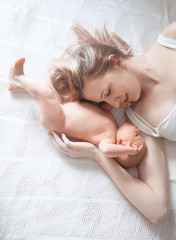 happy mom hugs her newborn daughter lying on the bed .