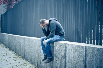 Unhappy depressed caucasian male sitting on urban street feeling