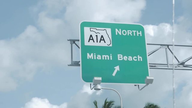 Road Signage on American highway going to North Miami Beach. Cloudy blue sky the day. Slow motion. RoadSign. Palm trees. Cars and skyscrapers. Close up.