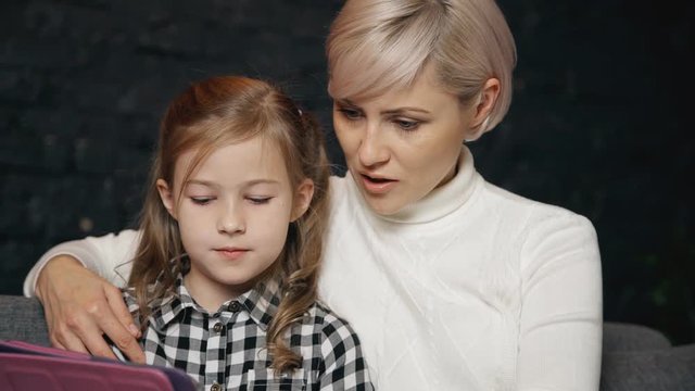 Relaxed mother using digital tablet with her charming daughter