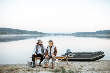 Grandfather with son sitting together on the bench while fishing on the lake early in the morning. Wide landscape view