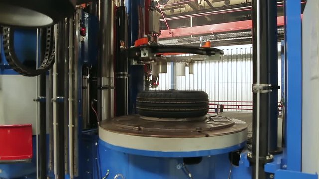 Tire production machine close up. Hot, smoked tires after molding arrive on the conveyor. Automotive wheel molding in a factory. Forming tire machine in action. Process of forming tires in a factory.