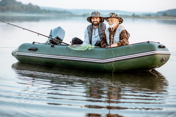 Portrait of a grandfather with adult son fishing on the inflatable boat on the lake early in the...