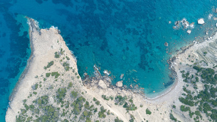 Aerial top view of sea waves hitting rocks on the beach with turquoise sea water. Amazing rock cliff seascape in the Greece coastline. Drone shot.
