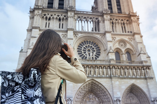 Young woman tourist photographing with camera standing in front of the famous Notre Dame cathedral in Paris