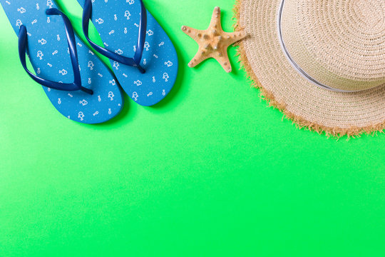Summer beach flat lay accessories. Sunscreen straw hat, flip flops and seashells on colored Background. Travel holiday concept with copy space