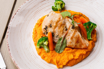 Chicken breast steak with carrot puree baby carrot and broccoli. Grilled chicken slice with baby carrot puree. wooden backgrounf