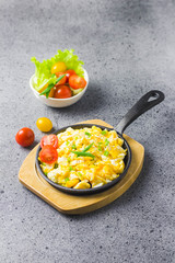 Soft creamy scrambled eggs in cast iron skillet and cherry tomatoes. Selective focus, space for text.