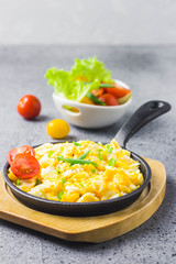 Soft creamy scrambled eggs in cast iron skillet and cherry tomatoes. Selective focus, space for text.