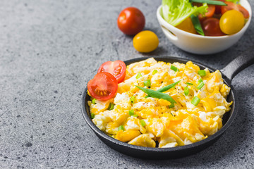 Soft creamy scrambled eggs in cast iron skillet and cherry tomatoes. Selective focus, space for...