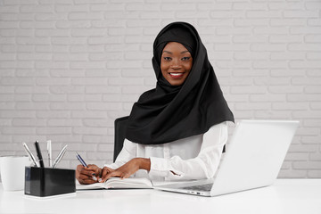 African muslim woman in black hijab posing at workplace.