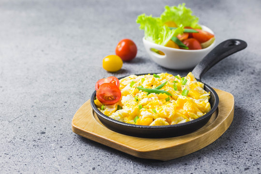 Soft creamy scrambled eggs in cast iron skillet and cherry tomatoes. Selective focus, space for text.