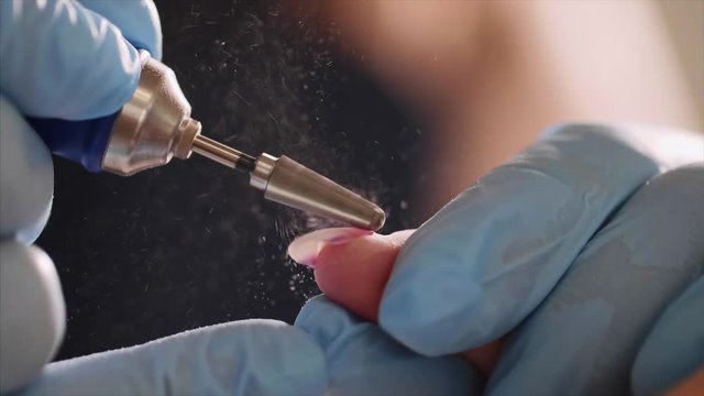 Manicurist does hardware manicure in the beauty salon in slow motion. Removal of the gel varnish with a milling cutter, finger closeup.