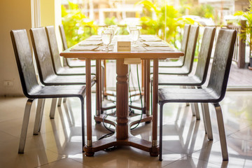 The tables and chairs in the restaurant with full set preparation next to the window with flare in the afternoon. 