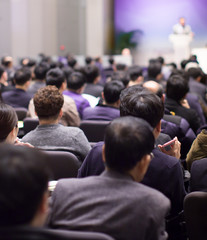 Speaker giving speech at business seminar in auditorium. Background of presenter in hall meeting during public lecture. Defocused businessman in conference hall with bokeh.