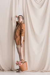 side view of fashionable model carrying flowers in bag standing on curtain background