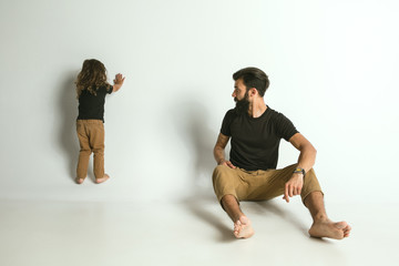 Father playing with young son against white studio background. Young dad having fun with his children in holidays or weekend. Concept of parenthood, childhood, father's day and family relationship.