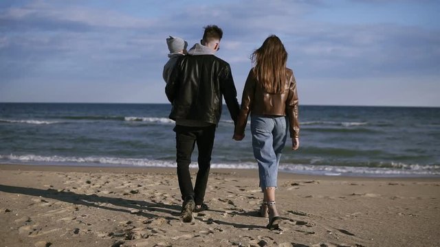 Young family, a father with his son on his arms, walks along the shore of the swa, on the coast. A happy family walks along the seashore and holding hands. Rare view