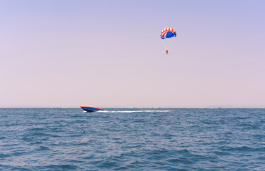 Ocean view of a man Parasailing in the sea towed by a speedboat in american colors - Watersports summer activity of a boat towing a parasail above water at twilight with USA stars & stripes - image