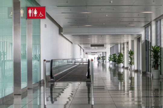 Empty hallway in airport hall with mobile walkway and toilet entrances.