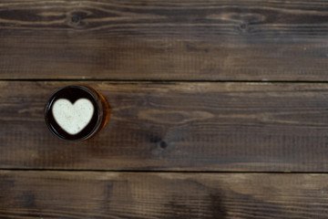 Mug of beer with silhouettes of a heart on dark wooden background. Empty space for text
