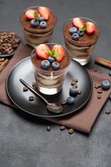 Classic tiramisu dessert with blueberries and strawberries in a glass on stone serving board on dark concrete background