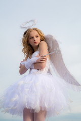 A child in the clothes of an angel on sky background - Valentine concept. Child with angelic character. Little angel girl against sunny sky.